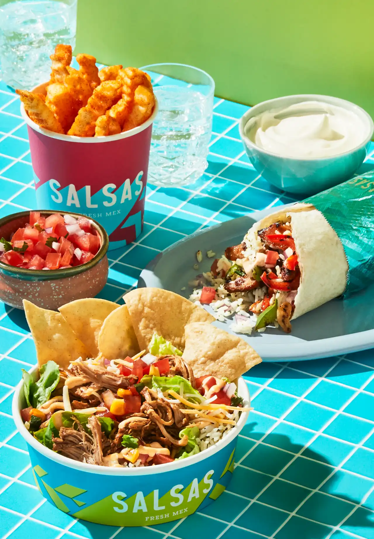 A Salsas spread of a burrito, bowl, fries, chips and salsa